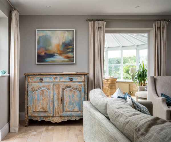 antique cabinet and modern painting in a country house. Corner sofa in blues and greys