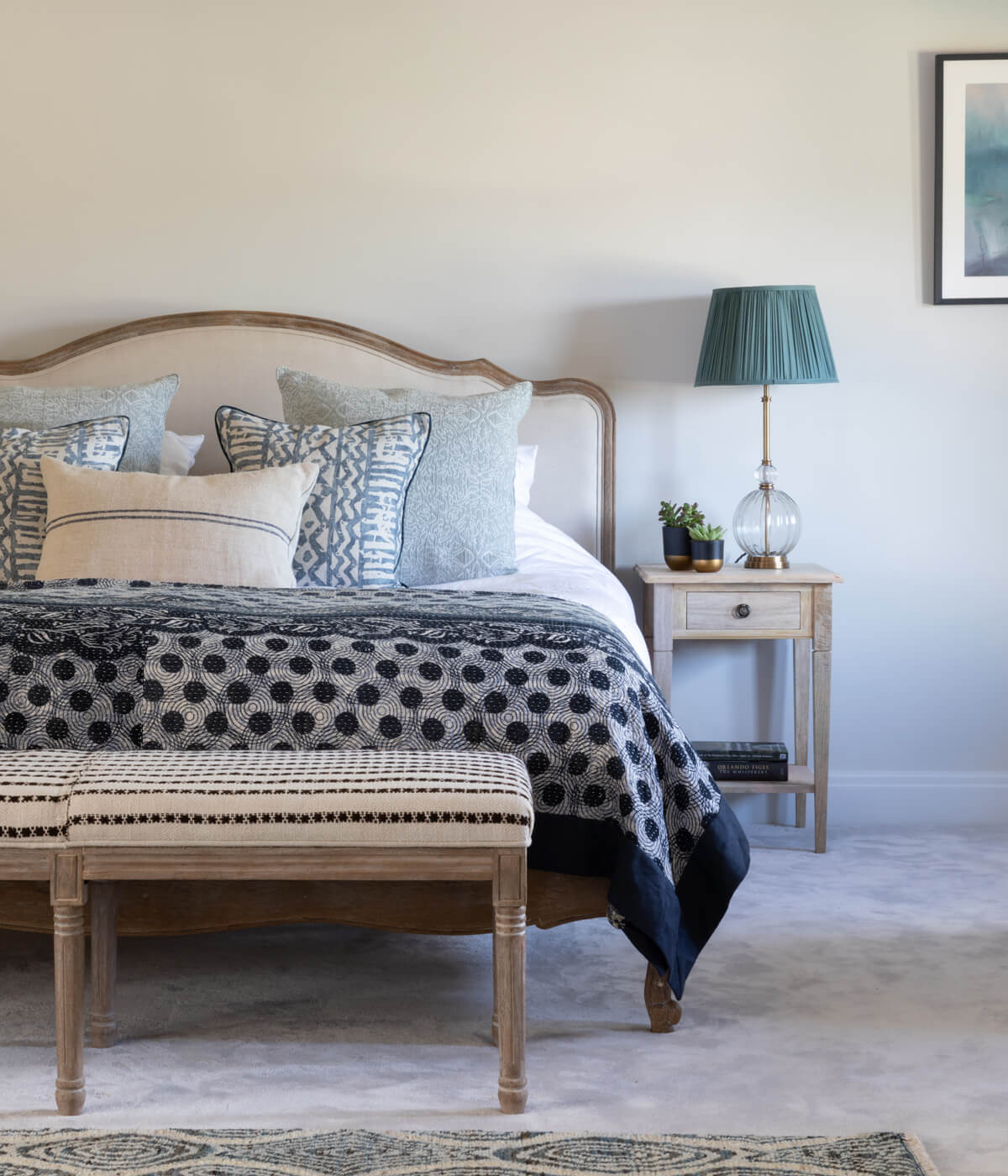 Master bedroom in blues and greys with natural wood beams. grey carpet and walls. Wood furniture and untie textiles on the bench