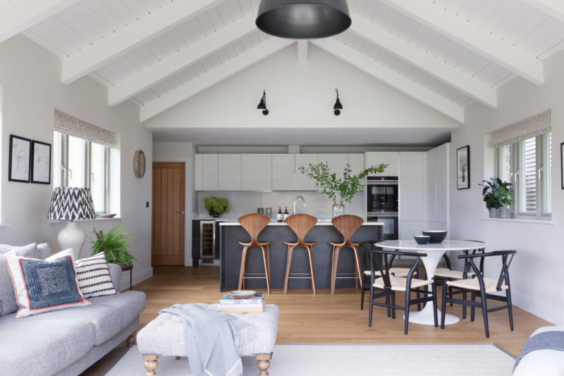 Modern kitchen in a barn conversions with sofa, footstool and chaise. Round dining table in white, black dining chairs