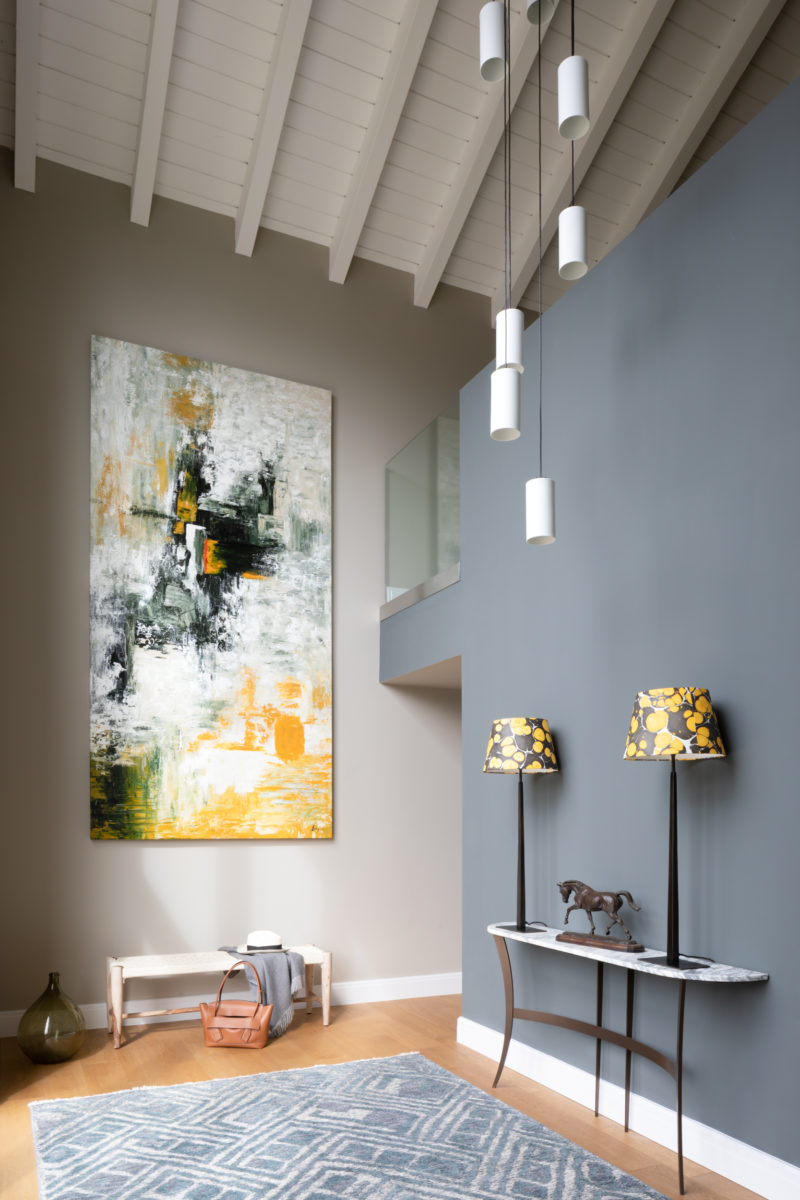 large artwork in galleried hall. Tall table lamps in console table under multi pendant light