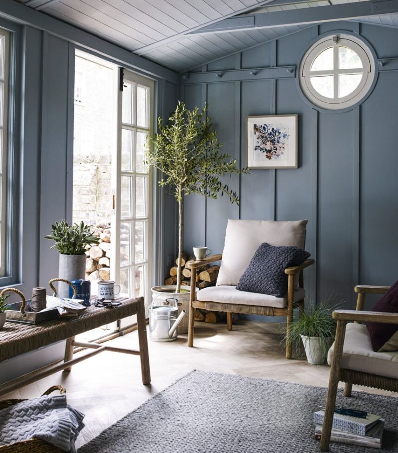 Blue walls for garden room with wood frame chair and French doors to garden