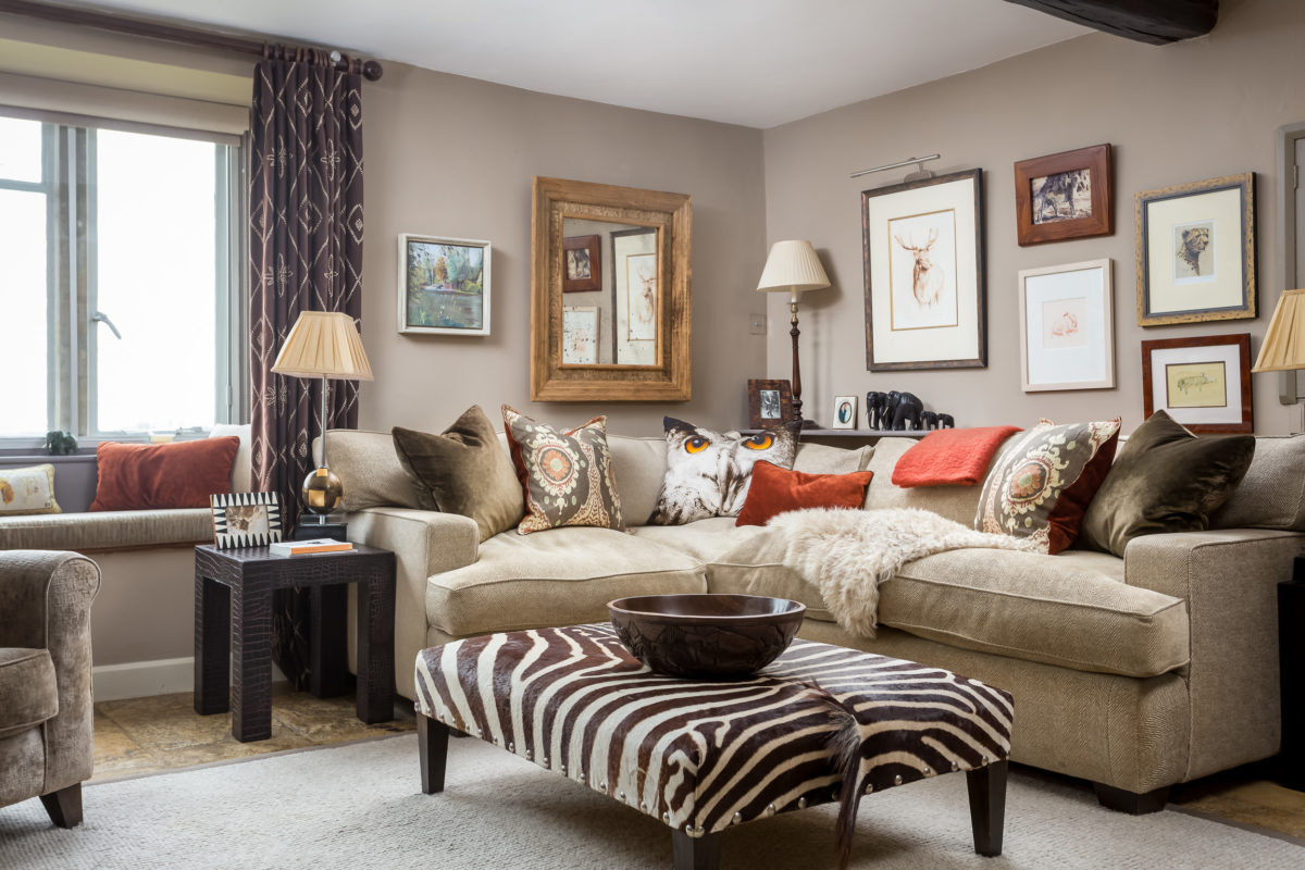 corner sofa with cushions in burnt orange & olive green. Pictures in groups on wall