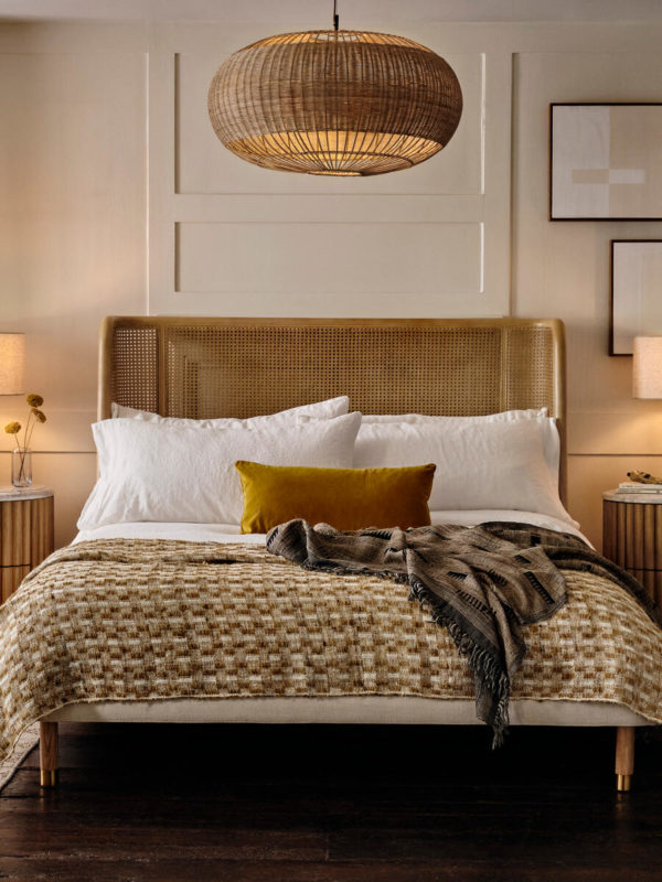 Cane pendant light in bedroom over rattan bed, mustard weave throw & velvet cushions