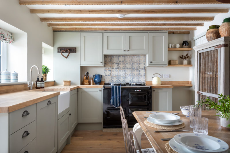 Country cottage kitchen in neutral tones with wood floor and wood beams. Aga with tiled splash back