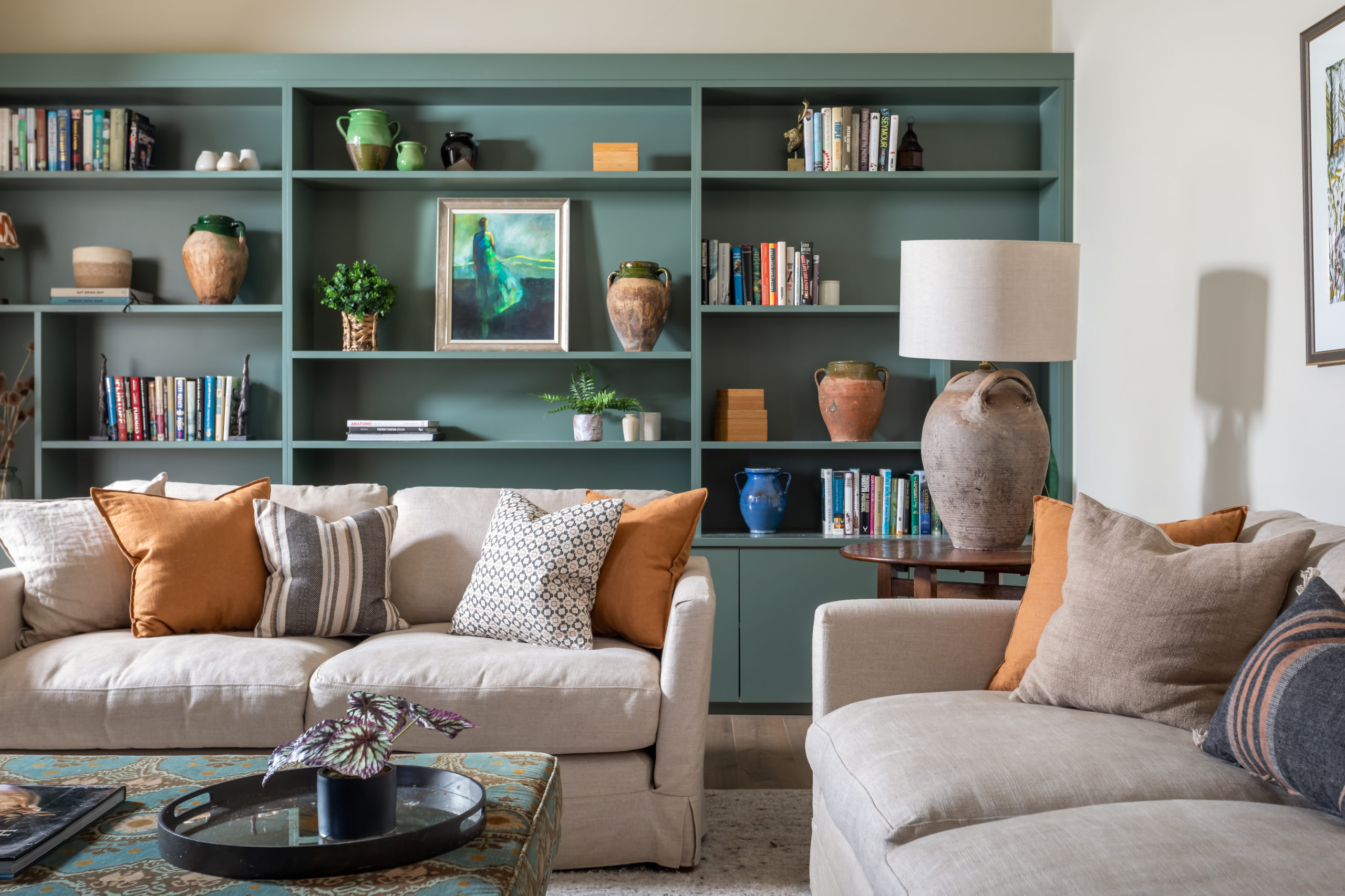 Bespoke bookcase painted green smoke. Neutral sofas and large patterned footstool.
