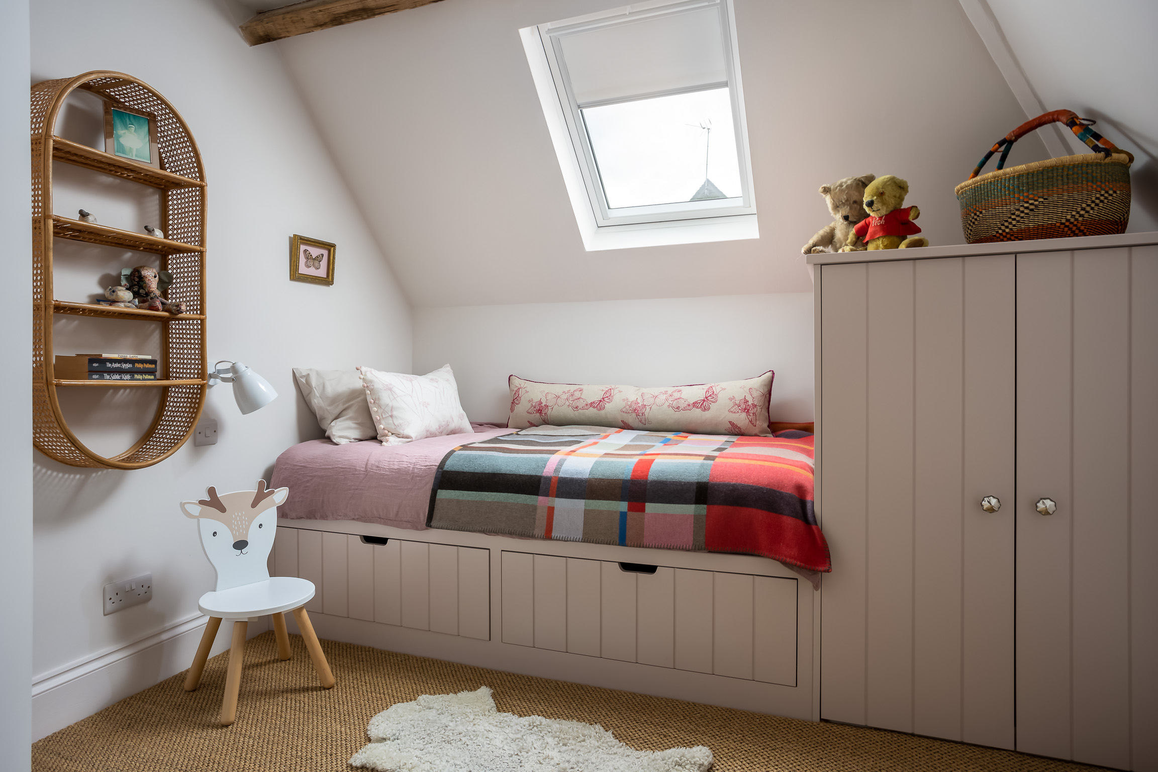 Girl's bedroom with pale pink walls, built-in bed and wardrobe. Sisal floor, wall mounted bedside lamp.