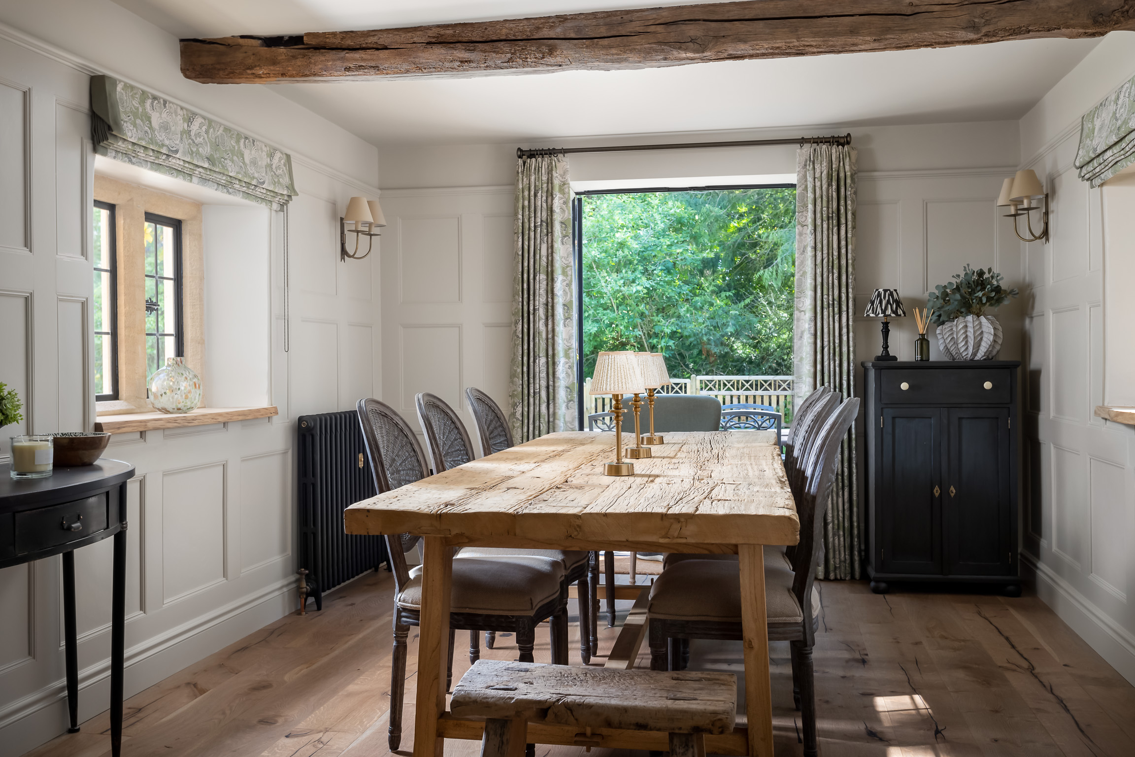 Wood dining table & oak dining chairs. Wall lights and battery lamps. Painted wood panelled walls.