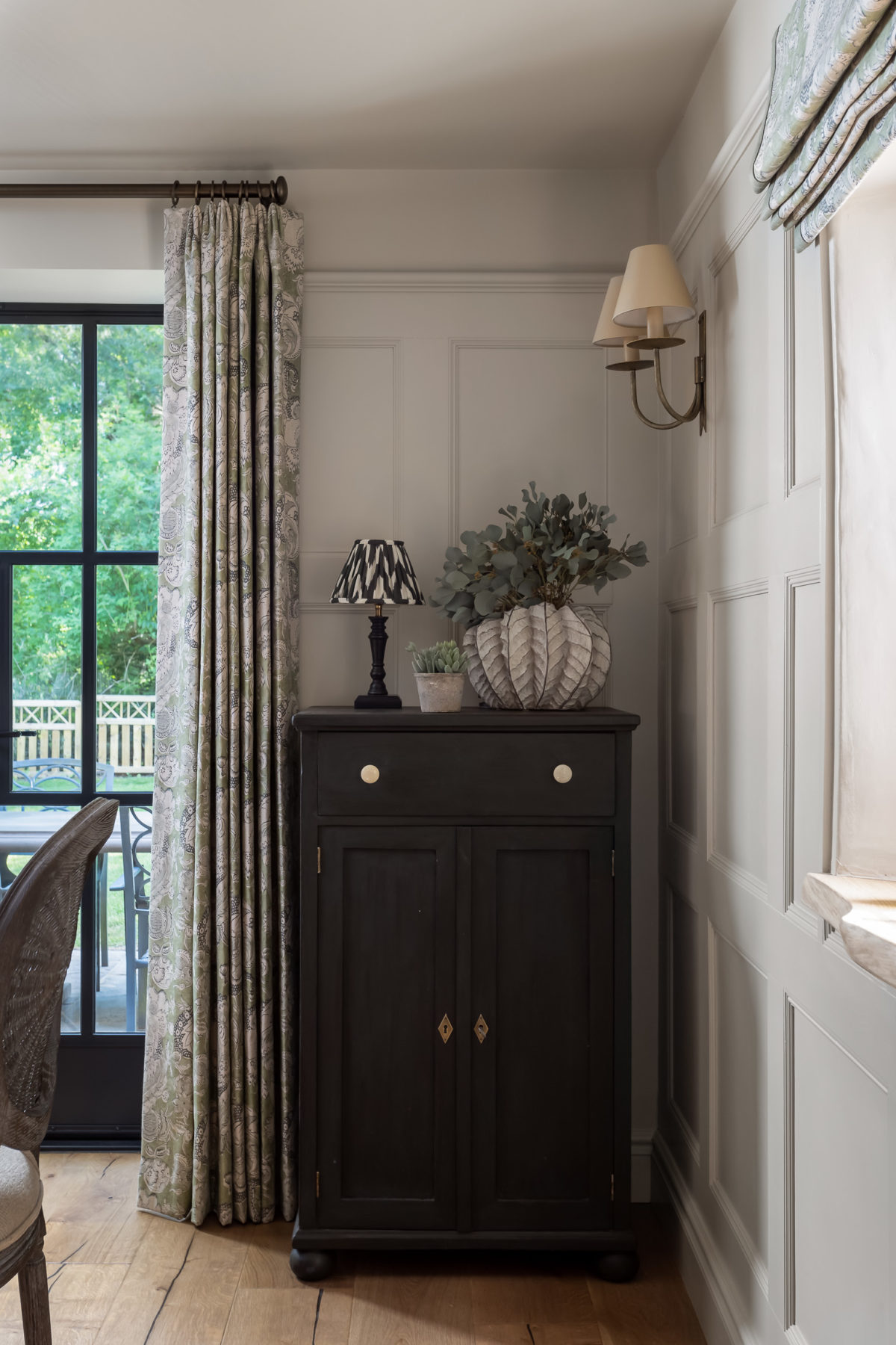 Wood panelled walls, wall lights, painted black sideboard, Crittal French doors & curtains