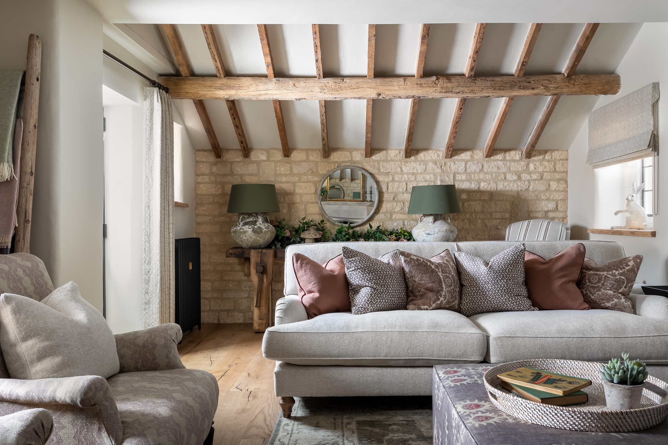 Wood beams in living room. Statement lamps, wood floor, cushions, sofa & footstool