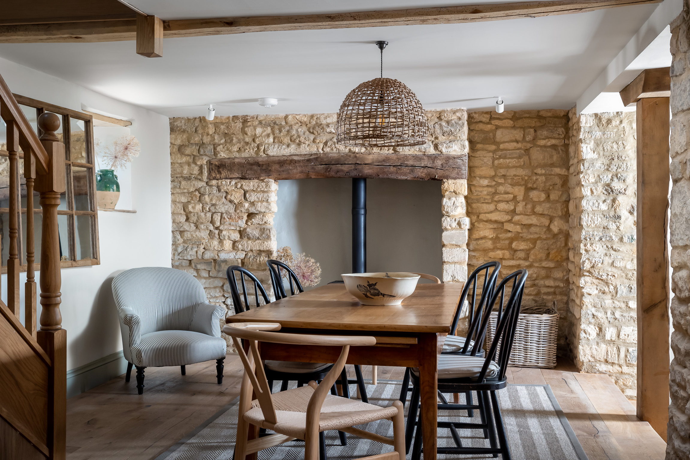 Oak dining table, painted black dining chairs, washable sisal rug on wood floor. Rattan pendant, Cosy fireside armchair