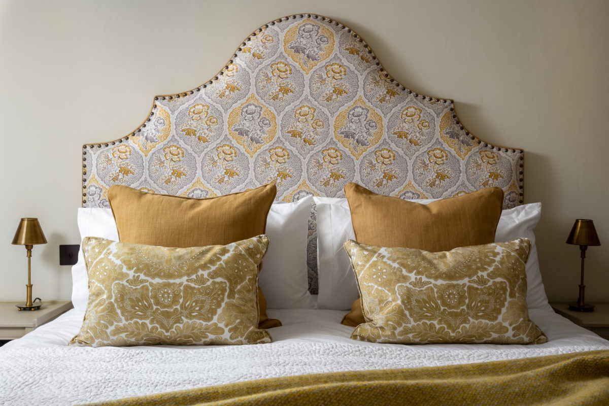 Ochre patterned & shaped headboard with velvet cushions on bed