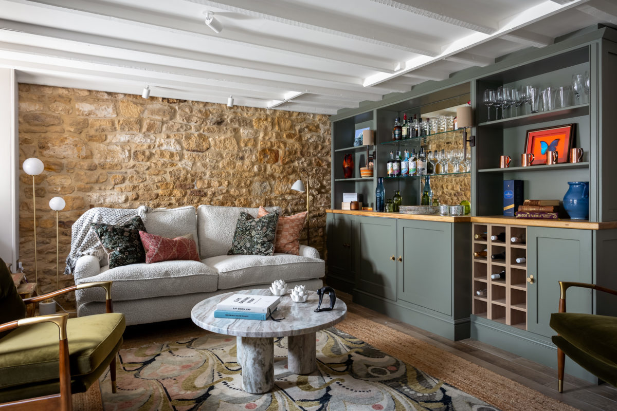 Bar room with cream boucle sofa, large rug, marble coffee table, green built in bar cabinet with mirror back, stone wall