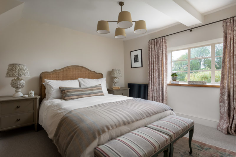 Bedroom with rattan h headboard to king bed, pink & earth tones, Jon Lawrence pendant light. Stool at door of bed