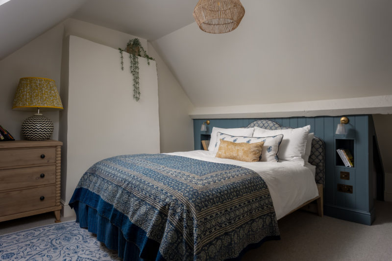 Attic bedroom with king bed & blue suzani. Wood panelling behind bed, rattan pendant light