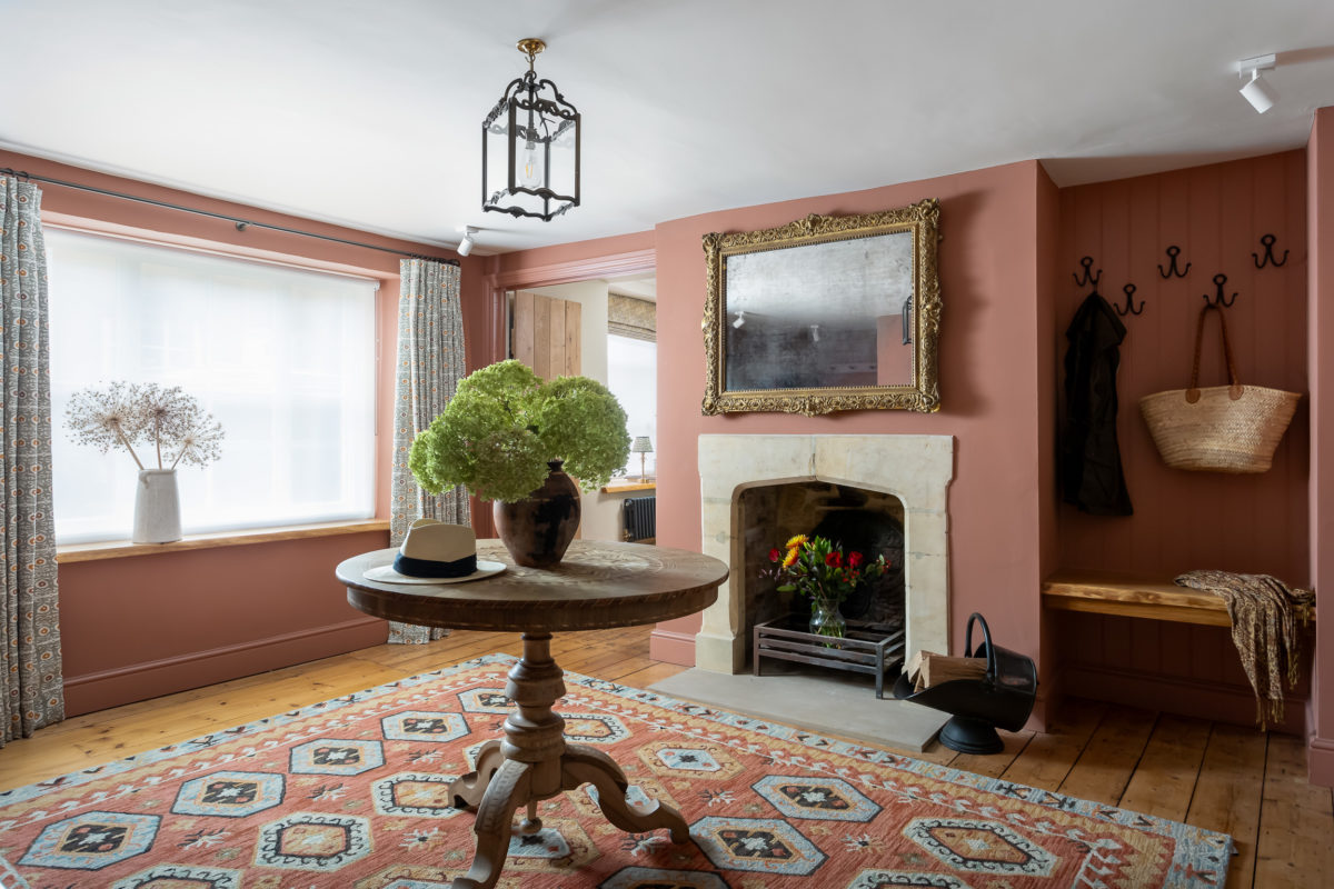 Terracotta entrance hall with large rug, walnut parquet pedestal table, pendant lamp over, stone fireplace & antique overmantel