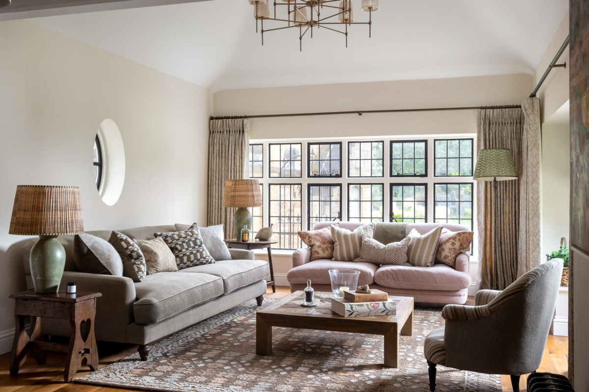 Green, brown & pink family room with brown and pink rug, green sofa, pink sofa, cushions, reclaimed wood coffee table, curtains on bronze pole