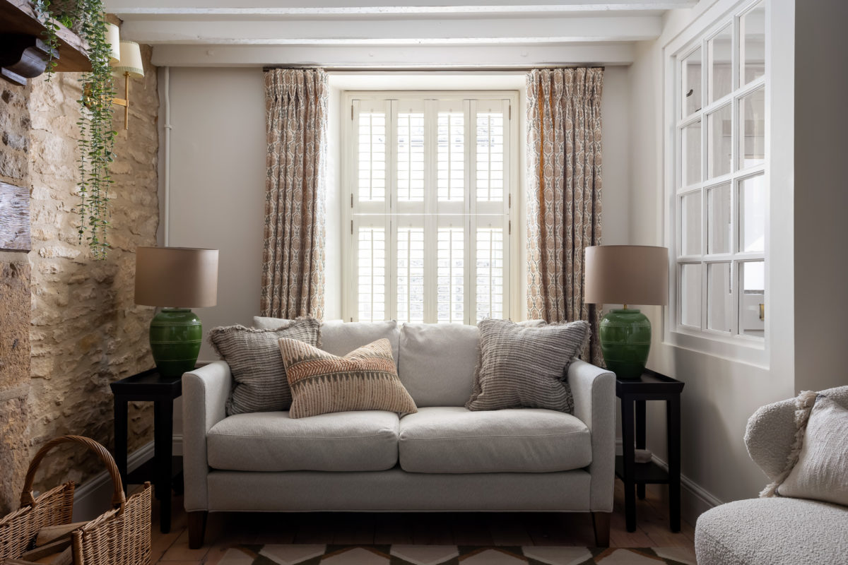 Neutral sofa with green & orange cushions. Interlined curtains & shutters, Green glass side lamps with taupe silk shades. Green pattern rug