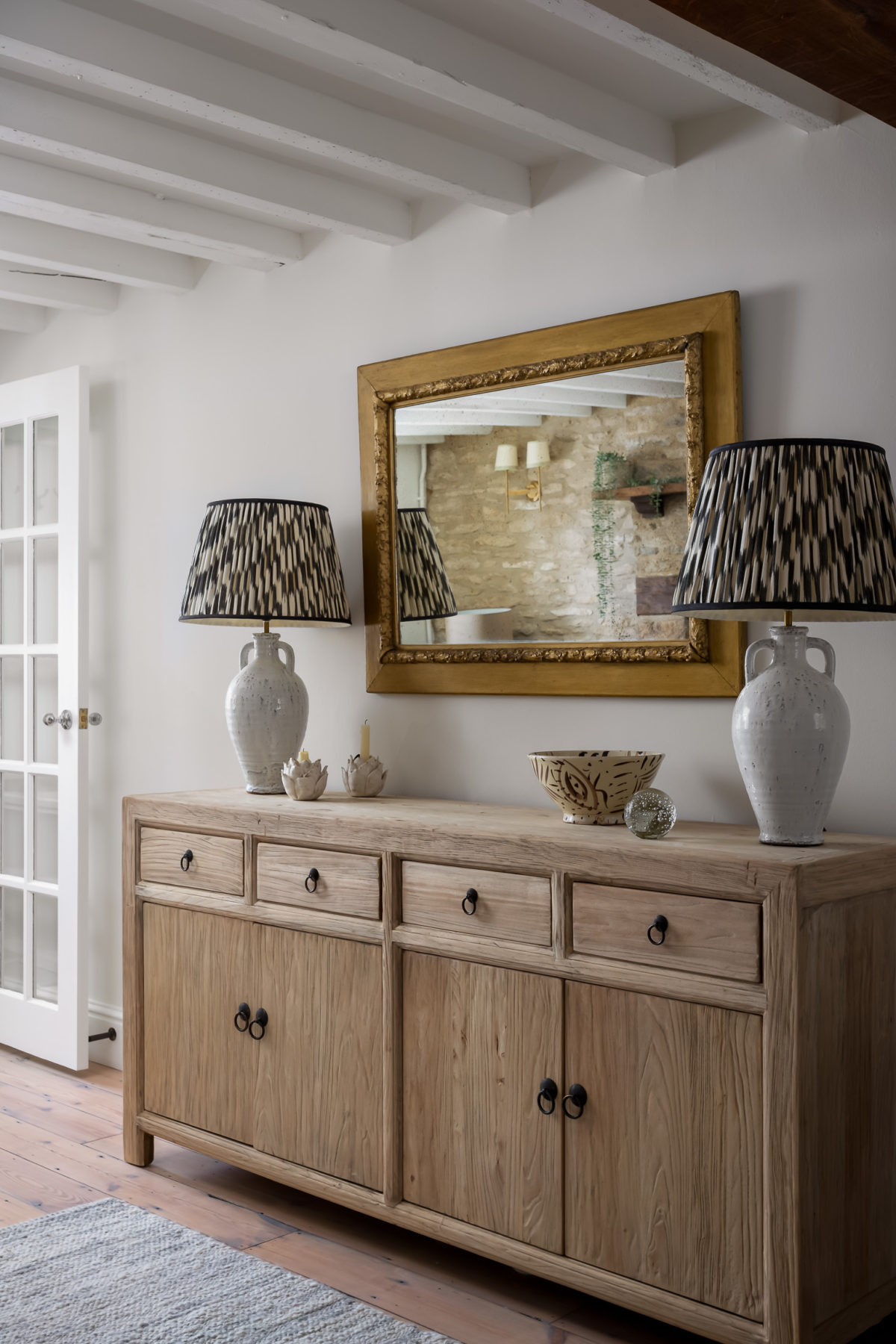 Sideboard in reclaimed wood with large antique mirror above and table lamps. Neutral wool rug