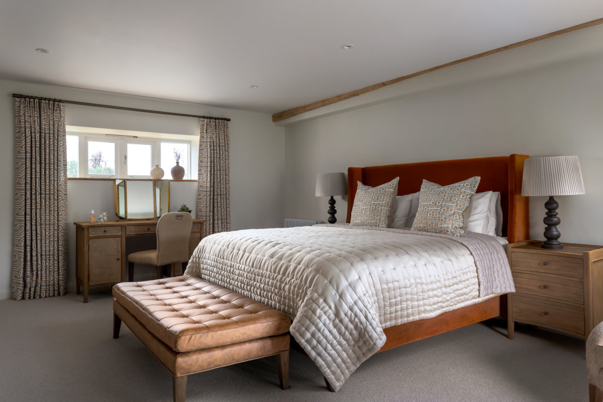 Bedroom with burnt orange upholstered headboard; leather footstool, dressing table & stool, bedside table with lamps